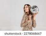 Beautiful woman in golden dress with disco ball posing on white background, space for text