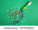 Beautiful serpentine and confetti bursting out of party popper on green background, flat lay