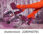 Small photo of Woman in orange tights and pink high heeled shoes among disco balls indoors, closeup