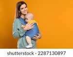 Small photo of Mother holding her child in sling (baby carrier) on orange background. Space for text