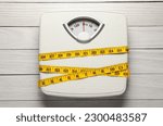 Small photo of Weigh scales tied with measuring tape on white wooden table, top view. Overweight concept