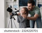 Little girl with his father looking at stars through telescope in room