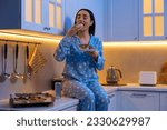 Small photo of Young woman eating donut in kitchen at night. Bad habit