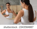 Small photo of Beautiful young woman doing breast self-examination near mirror in bathroom