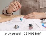 Astrologer using natal chart and pendulum for making forecast of fate at table, closeup. Fortune telling