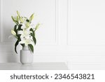 Beautiful bouquet of lily flowers in vase on light table near white wall, space for text