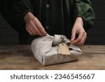 Furoshiki technique. Woman wrapping gift in fabric at wooden table, closeup