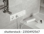 Hairdryer plugged into power socket on light grey wall in bathroom
