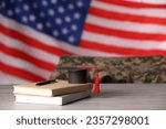 Small photo of Notebooks, mortarboard and pen on wooden table against flag of USA, space for text. Military education