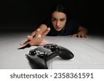 Gaming disorder. Woman reaching out for gamepad on floor from darkness