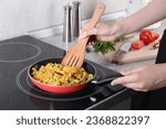 Woman frying rice with meat and vegetables on induction stove in kitchen, closeup