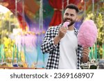 Happy young man eating cotton candy at funfair, space for text