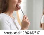 Woman brushing her tongue with cleaner on blurred background, closeup. Space for text