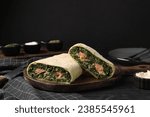 Tasty strudel with salmon and spinach on black wooden table
