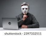 Small photo of Man in mask showing hush gesture at white table with laptop against grey background