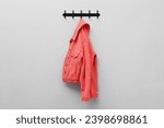 Coral jacket hanging on coat rack on light grey wall