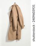 Small photo of Beige trench coat hanging on hook rack on white wall
