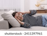 Sad woman suffering from headache on sofa indoors