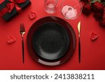 Place setting with heart shaped candles, gift box and bouquet of roses on red table, flat lay. Romantic dinner