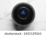 Small photo of Magic eight ball with prediction Answer Unclear Ask Later on white marble table, top view
