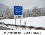 Snow is falling around a sign for European border, frontier between Germany and Austria. The sign says: 