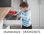 Little boy opening drawer with cutlery at home