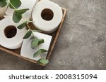 Basket with rolls of toilet paper and eucalyptus branch on grunge background