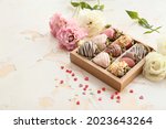 Box with tasty glazed strawberry and flowers on light background