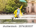 Small photo of Young Asian man in raincoat and with umbrella on city street