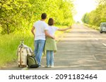 Young couple with suitcase hitchhiking on road