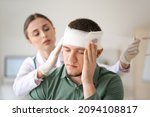 Doctor applying bandage onto head of young man in clinic
