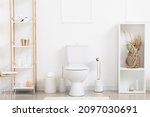 Interior of light restroom with toilet bowl, paper holder and shelf units
