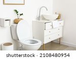 White toilet bowl and chest of drawers near light wall in restroom