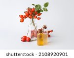 Bottles of essential oil and rose hip berries isolated on white background