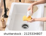 Housewife pouring detergent onto sponge over sink in kitchen, closeup