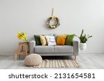 Small photo of Comfortable sofa near light wall with Easter wreath in living room interior