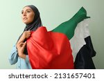 Beautiful Muslim woman with waving UAE flag on green background