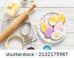 Plate with tasty Easter cookies and ingredients on white wooden background