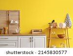 Modern shelving unit with dishware and kitchen counter near yellow wall