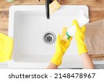 Woman in rubber gloves pouring detergent onto cleaning sponge near sink