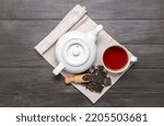 Small photo of Napkin with scoop of dry puer tea, cup and teapot on dark wooden background