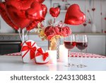 Dining table with gifts, glasses of wine, candles, flowers and balloons for Valentine's Day in kitchen