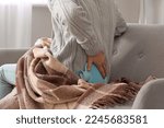 Small photo of Young man warming his lower back with hot water bottle on sofa at home