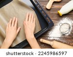 Woman putting paper into baking sheet on wooden background