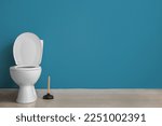 Ceramic toilet bowl and plunger near blue wall
