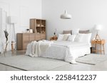 Small photo of Interior of bedroom with bed, shelving unit, burning candles and houseplants near white wall