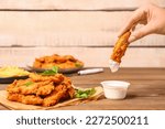 Small photo of Woman dipping tasty nugget into sauce on wooden table