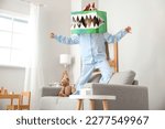 Small photo of Little boy in cardboard dinosaur costume playing at home