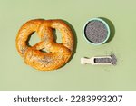 Tasty pretzel and bowl of poppy seeds on color background