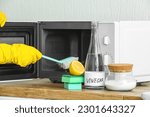 Woman cleaning microwave oven with brush, baking, soda and vinegar at home